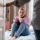 Sad teen girl sits on bed while parent enters room